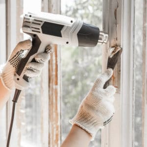 heat gun and scraper being used to remove paint from window frame