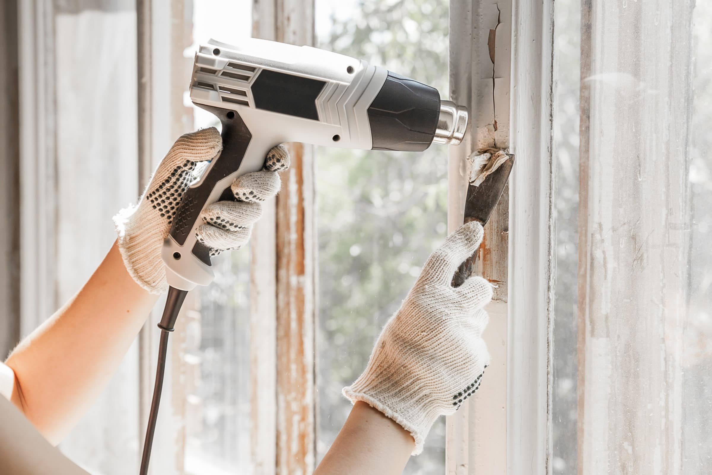 heat gun and scraper being used to remove paint from window frame